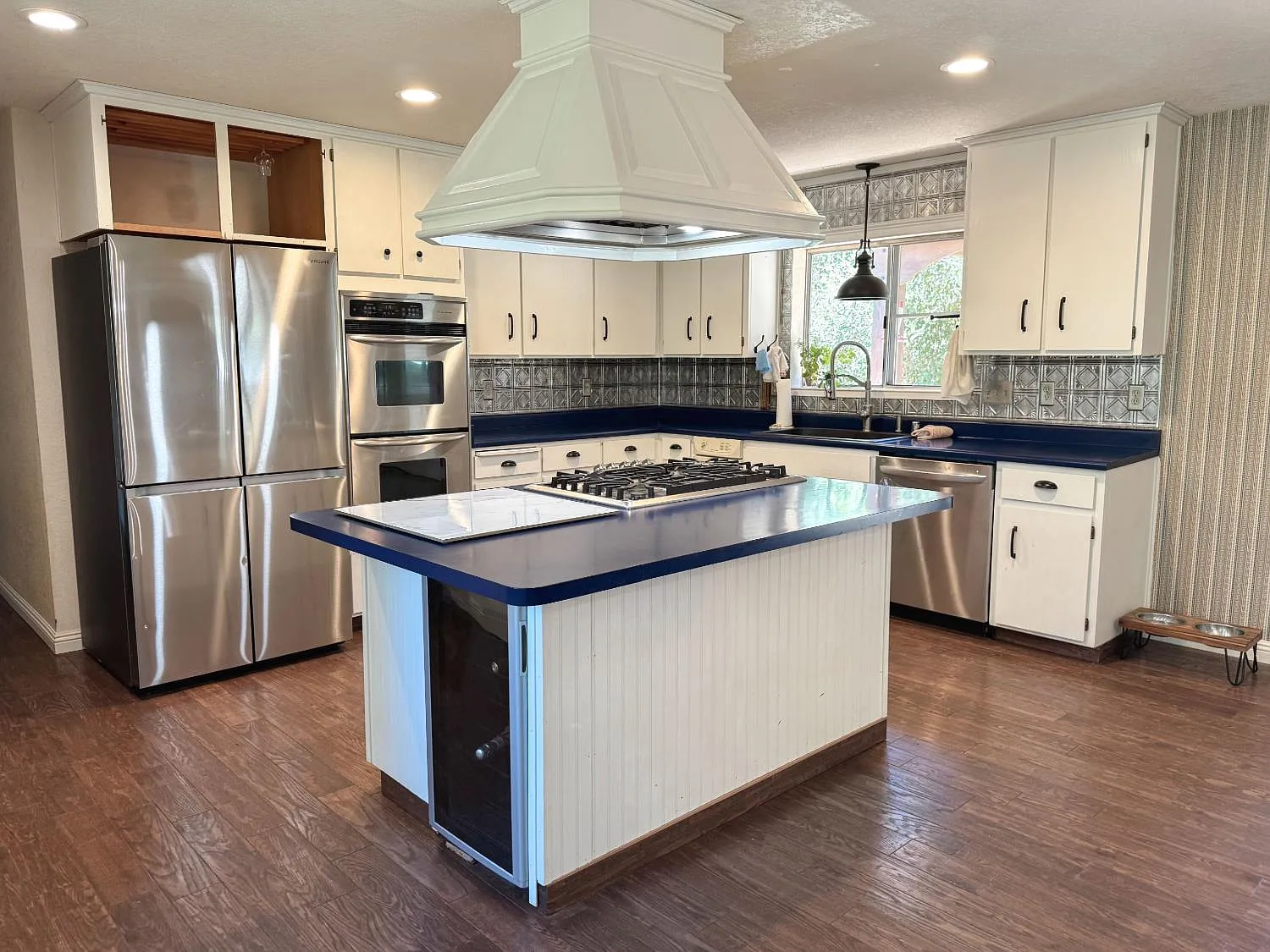 Kitchen island with five-burner gas cooktop, stainless refrigerator and built-in ovens
