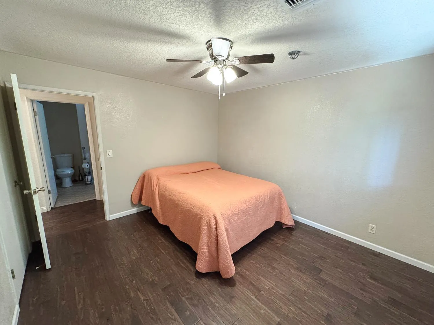 Bedroom with dark wood flooring, ceiling fan and ensuite door