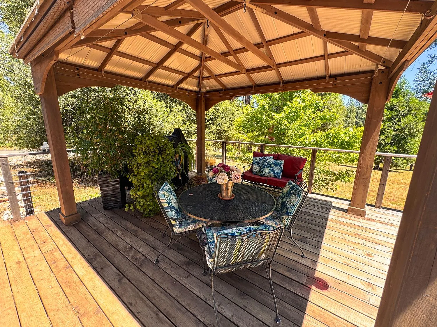 Timber-framed gazebo on the deck with outdoor table and seating, looking out to pines